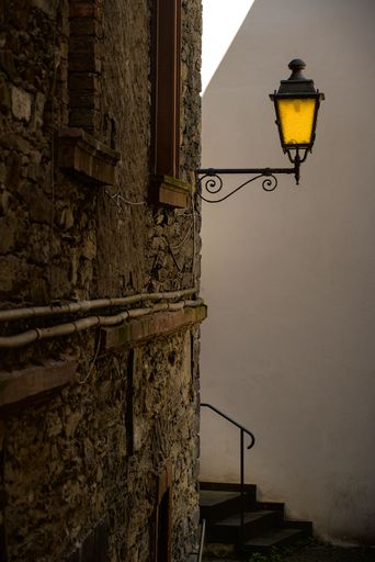 A vertical shot of decorative old yellow lamp on a wrought iron post fixed at a stone wall of an old house