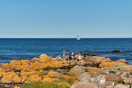 Aarsdale, Bornholm island, Denmark - June 28, 2019. Group of tourists spending their time on rocky coast of Baltic sea in Aarsdale.