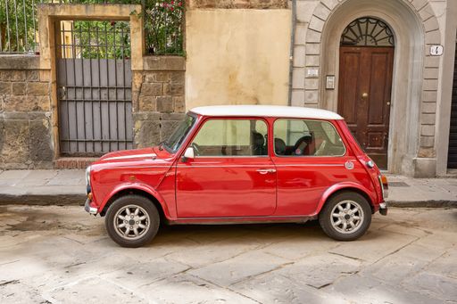 A red and white automobile parked in front of an iconic Italian building