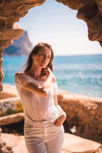 A young attractive woman from Spain dressed in white by the sea, in a stone window