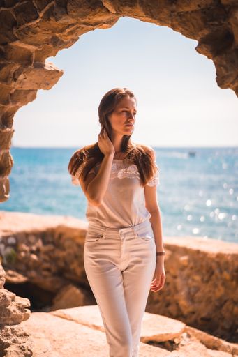 A young attractive woman from Spain dressed in white posing for the camera by the sea in a stone window
