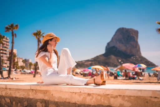A young attractive woman from Spain dressed in white and with a straw hat resting on the beaches of Calpe, Valencia, Spain