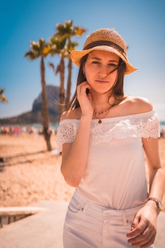 A young attractive woman from Spain dressed in white with a straw hat looking at the camera on the beaches of Calpe, Valencia, Spain