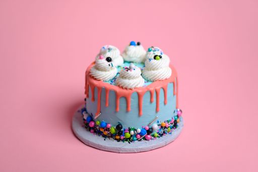 A blue birthday cake with white cream meringues and sprinkles against a pink background