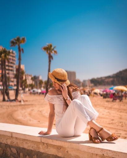 A young redhead from Spain dressed in white with a straw hat posingon the beaches of Calpe, Valencia, Spain