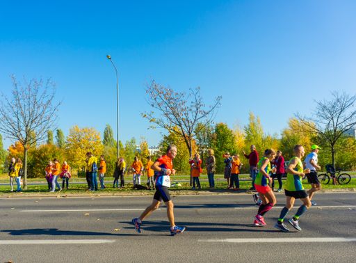 Many people running on street during the PKO Poznan Marathon on a sunny day in the autumn season.  The event is sponsored by many different companies.
