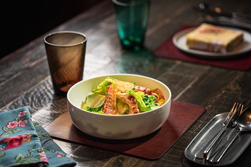 A closeup of a bowl of salad with greens and bacon on a wooden table