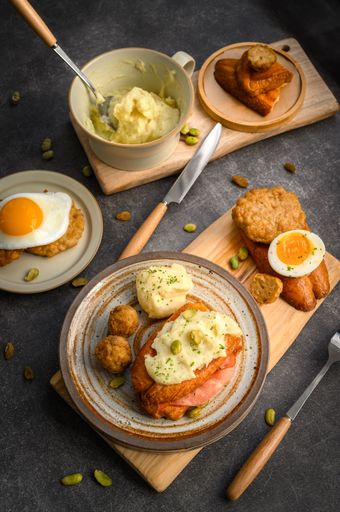 ceramic plates containing a single boiled egg, a slice of bread, and a bowl of mashed potatoes, arranged on a black tabletop