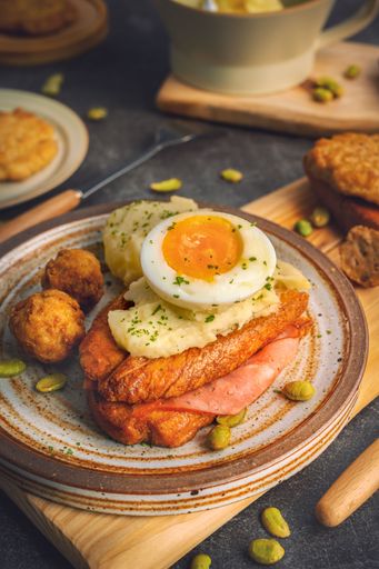 A rustic wooden board with breakfast including toasted bread, mashed potatoes, and boiled eggs