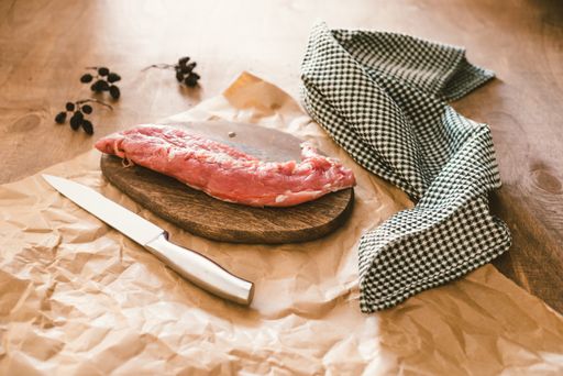 A piece of raw pork tenderloin on a chopping board with seasonings on the table