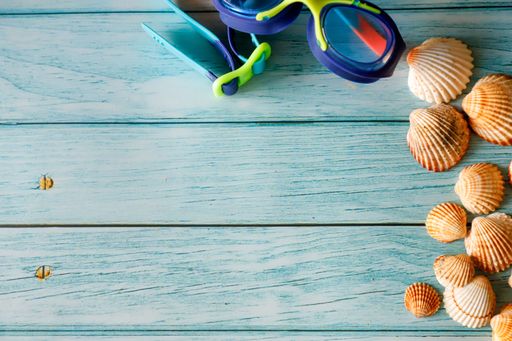 A wooden blue background with beautiful brown white seashells, swimming goggles, and copy space