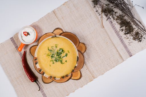 A top view of pumpkin soup in a bowl on round woodcuts served with chili pepper and salt