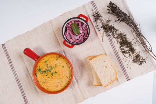 A top view of soup with greens served with onions in a bowl and white bread
