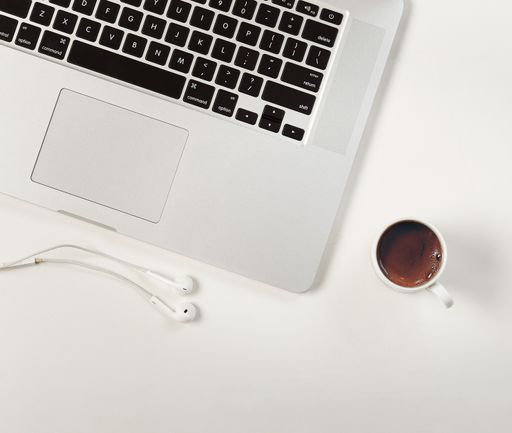 A top view of a cup of coffee next to a laptop with earphones