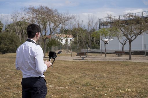 A young male in a flight school uniform piloting during a drone flight practice in a field with trees