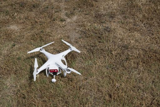 a high angle shot of a white drone isolated on the dry grass on the ground