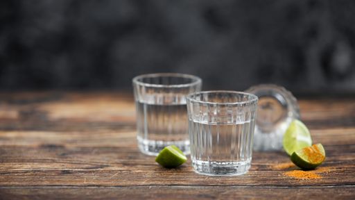 A closeup shot of a tequila shot with spicy pepper slices