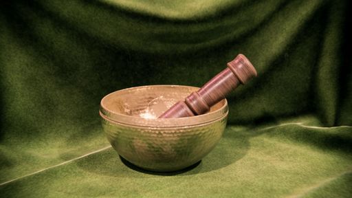An ornate, hand-crafted Tibetan singing bowl stands against vibrant green cloth