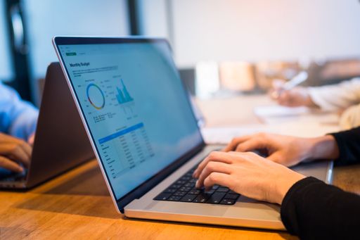 A female office worker working on a laptop computer from a wooden desk in a modern office environment