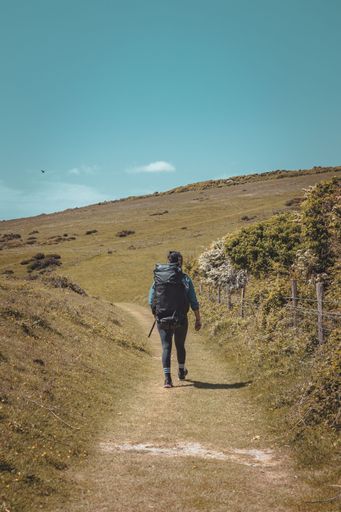 A person walking on a trail in a nature setting, heading towards a mountain range in the background