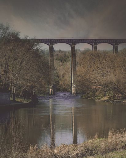 A vertical shot of the stone bridge over the river under a cloudy sky