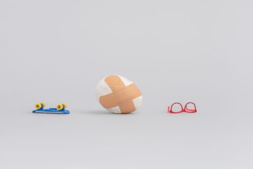 A lego skateboard, pink sunglasses and egg covered by medical tapes, laying on the ground isolated in white background
