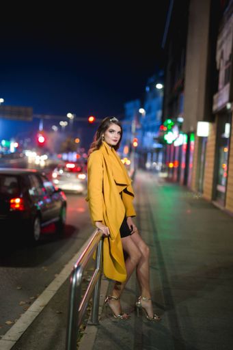 A vertical shot of a young blonde female model in a fashionable yellow coat