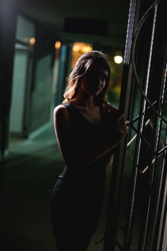A vertical shot of a young female model in an elegant black dress posing near a door at night