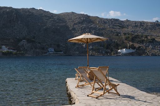 A closeup of wooden chairs situated on a rocky shoreline, surrounded by tranquil water in Greece