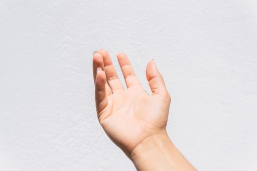 A closeup of asking hand sign against a white wall background