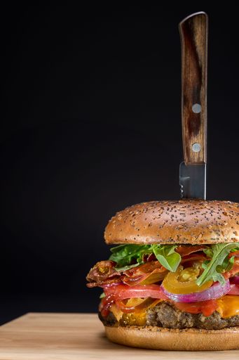 A closeup shot of a hamburger with a metal knife inserted in the center