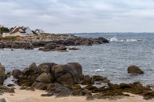 A landscape of a rocky shore surrounded by the water under a cloudy sky in the countrysid0e