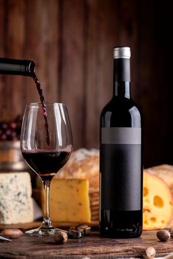 A vertical closeup of a bottle of red wine with a glass and cheese assortment