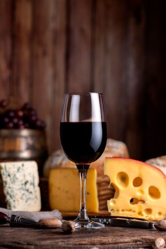 A vertical closeup of a glass of red wine with a cheese assortment