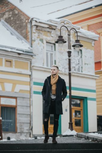 A vertical shot of a Caucasian fashionable sexy man with a brown scarf on the street lamp background