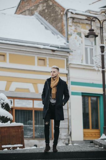 A vertical shot of a Caucasian fashionable sexy man with a brown scarf on the street lamp background