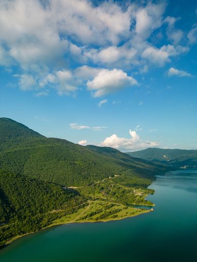 An aerial view of a lake surrounded by green mountains on a sunny day
