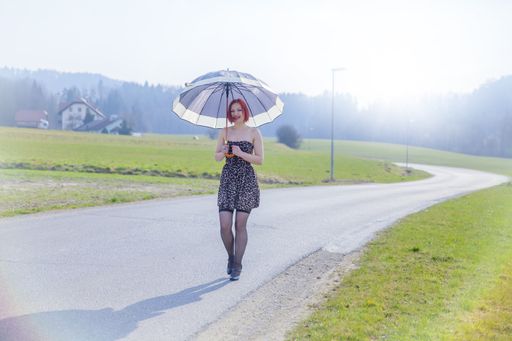 Young red hair female with umbrella walks by road on sunny day