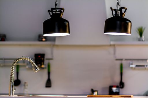A pair of black hanging lamps above a sink in a modern white kitchen