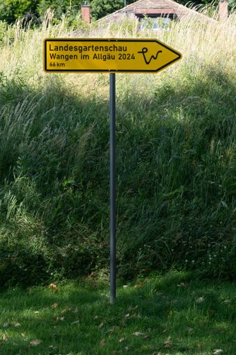 A yellow sign with text: state garden show, pointing to a grassy area.