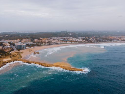 An aerial shot of foam waves hitting a sandy seashore