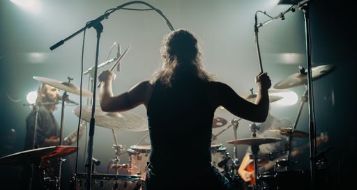 A man on a stage performing on the drums during a concert, shot from back