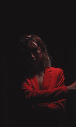 A female dressed in a red blazer with wet hair and smudged red lipstick in a dark room