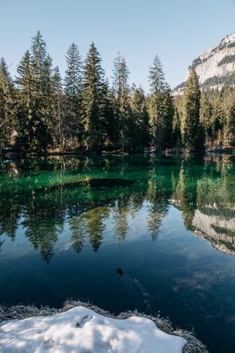 A vertical picture of a lake surrounded by rocks and forests with trees reflecting on the water