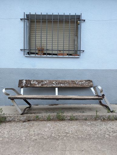 A wooden bench in a village under a window.