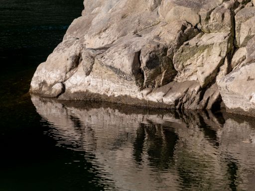 A closeup of a large rock and its reflection beside a still-dark river Otaki River, Kapiti Coast,