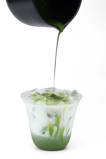 Pouring matcha into cup with ice and milk on a white background - process of making matcha tea