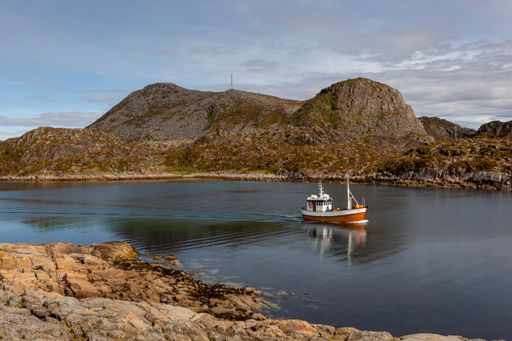 A sailboat is pictured on a body of water, surrounded by mountainous terrain and jagged rocks