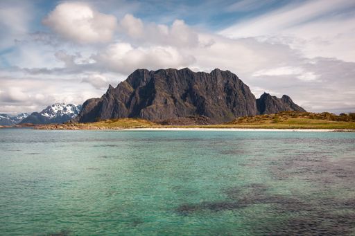 An idyllic landscape of a snow-dusted mountain overlooking a tranquil ocean with a body of water in the foreground