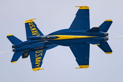A bright blue and yellow aircraft is soaring through the sky, leaving a white smoke trail in its wake